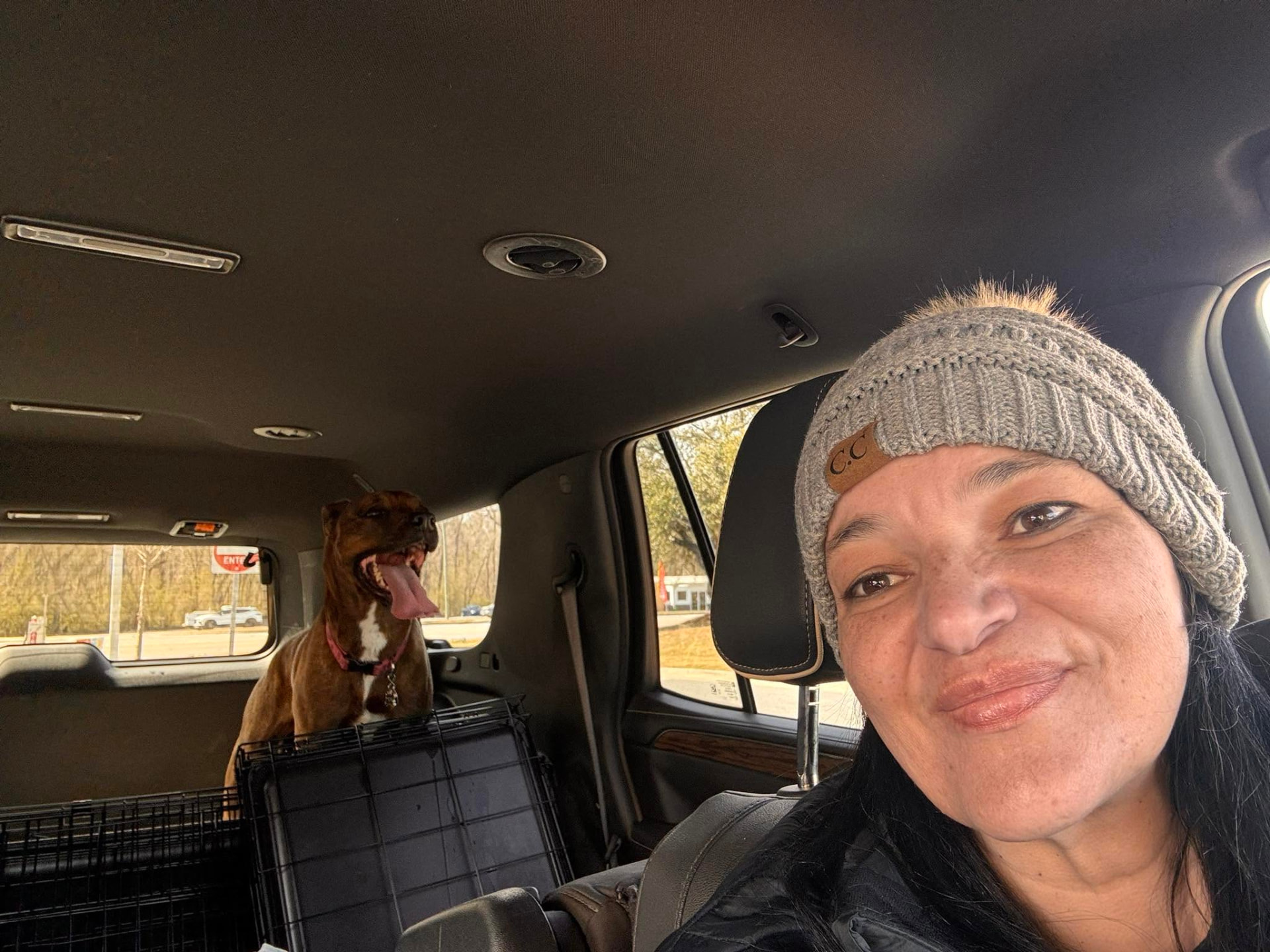 Miles For Smiles driver smiling in the transport vehicle with a happy brindle dog resting in its travel crate