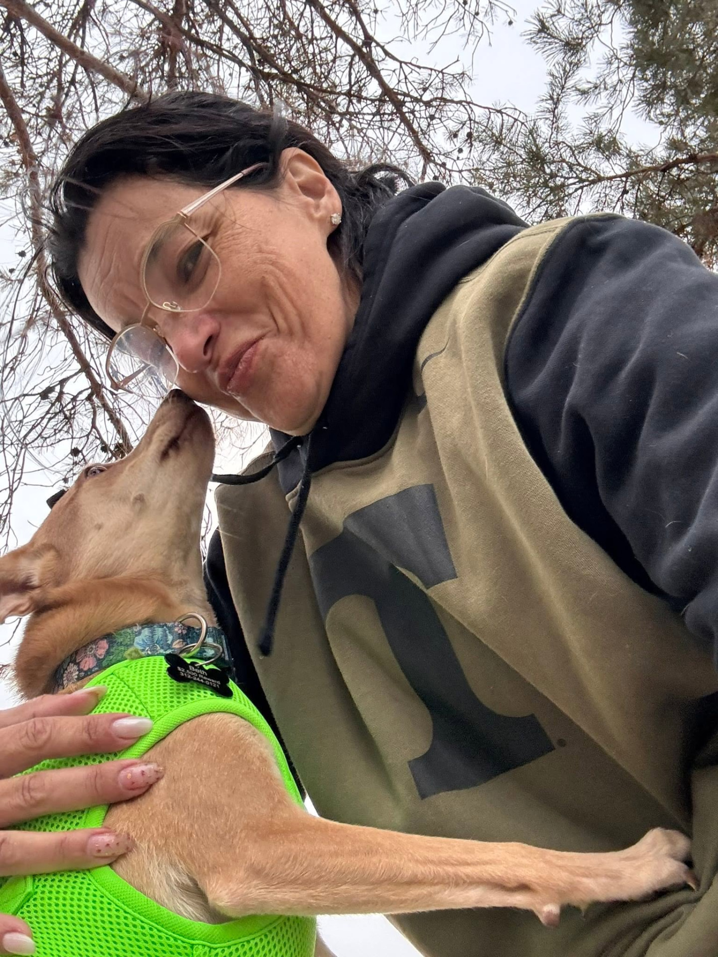 Caregiver bending down to comfort a tan dog in a green harness on a snowy walk