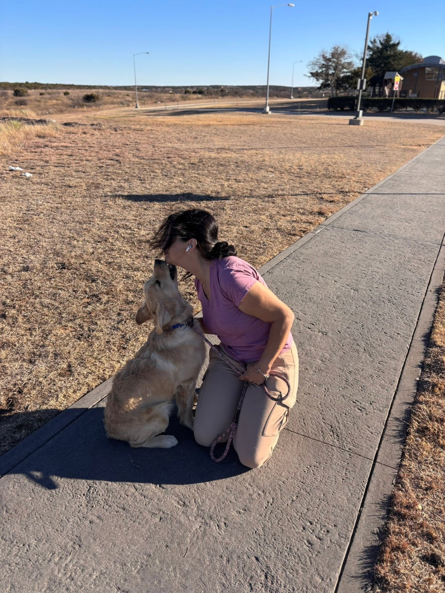 Golden retriever nose to nose with a caregiver kneeling on a sunny sidewalk during a rest stop